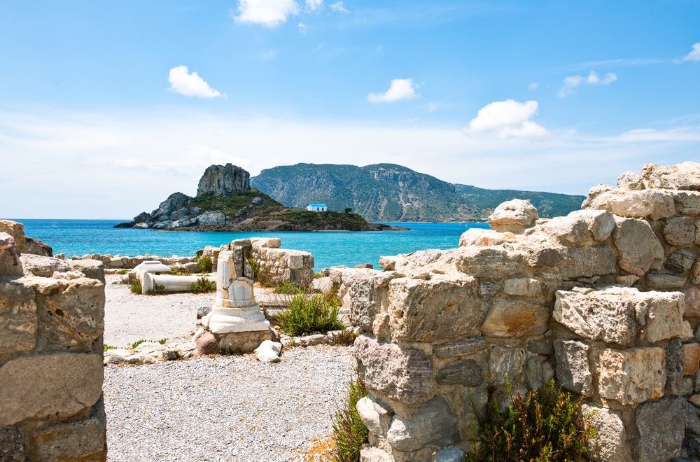 Ruiny starověkého řeckého chrámu s výhledem na tyrkysové moře a skalnatý ostrůvek, příklad bohaté historie a nádherné přírody v Řecku pro první návštěvníky