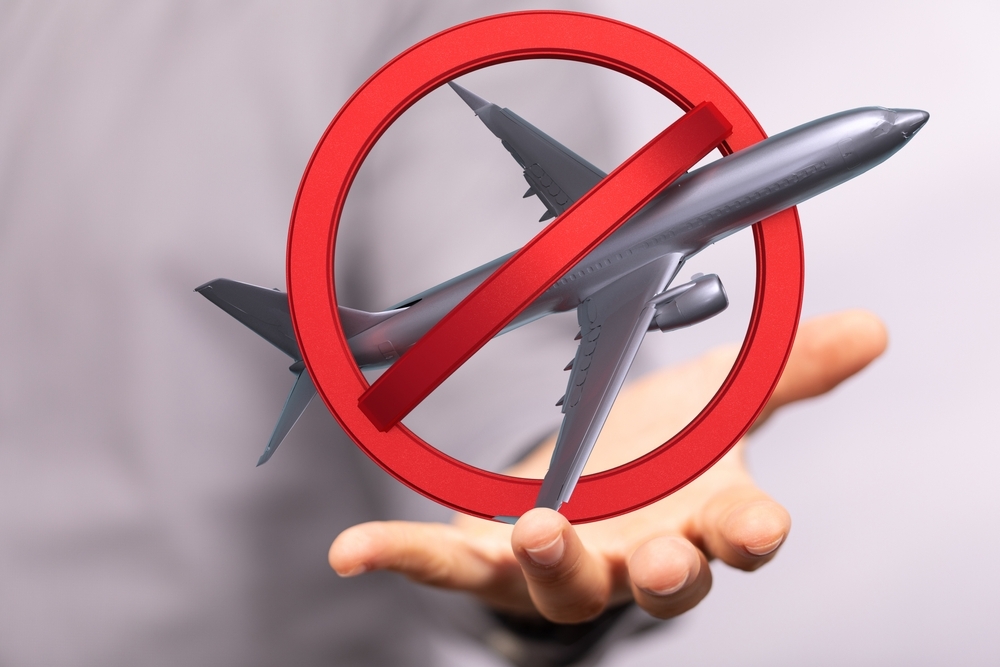Zakázané létání, model letadla překřížený červeným kruhem nad rukou, symbolika omezení cestování nebo letových zákazů