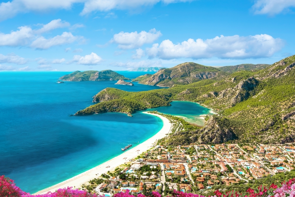 Malebný výhled na modrou lagunu s bílou písečnou pláží a zelenými kopci na Egejské riviéře v Turecku.