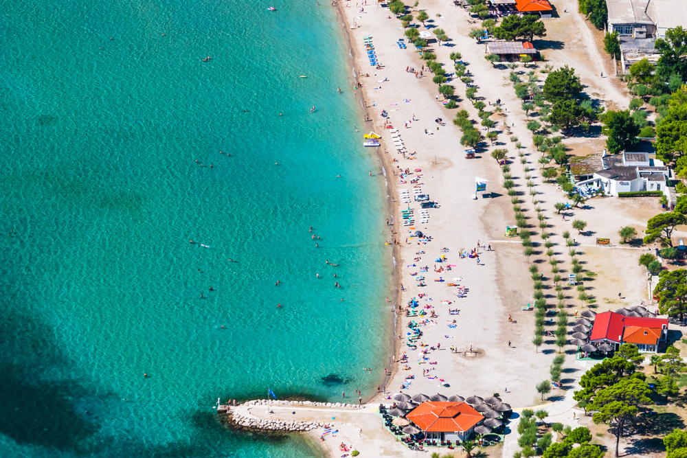 Lidé opalující se na pláži a koupající se v moři v Omiši v Chorvatsku
