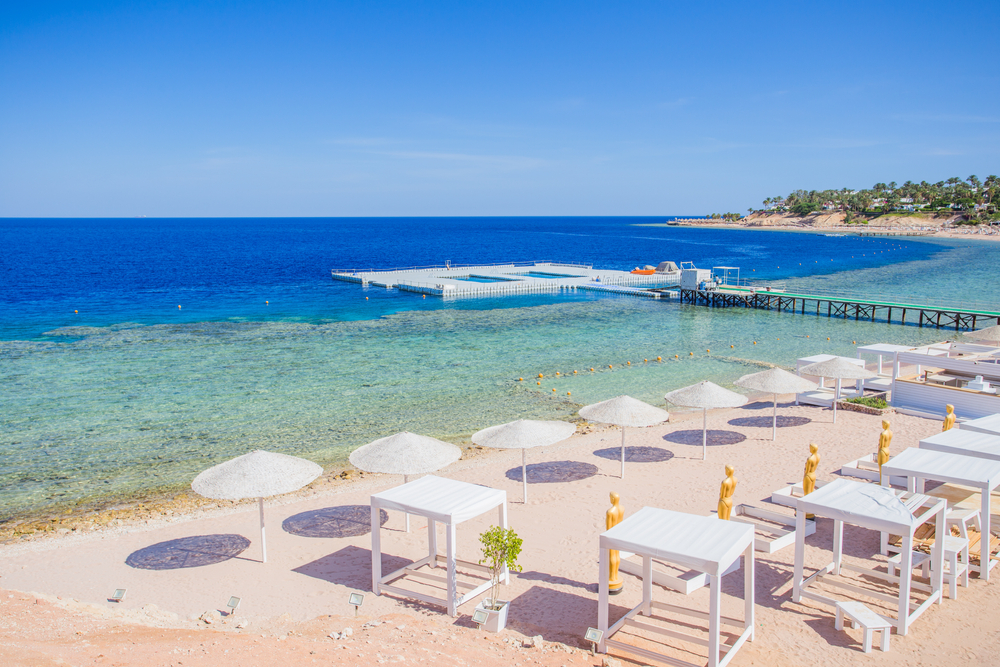 Malebná pláž s bílými slunečníky, průzračným mořem a molem