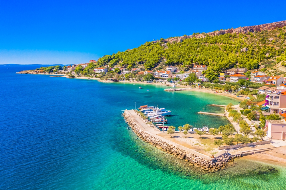 Pláž Duće v Chorvatsku s průzračnou tyrkysovou vodou, zelení a domky