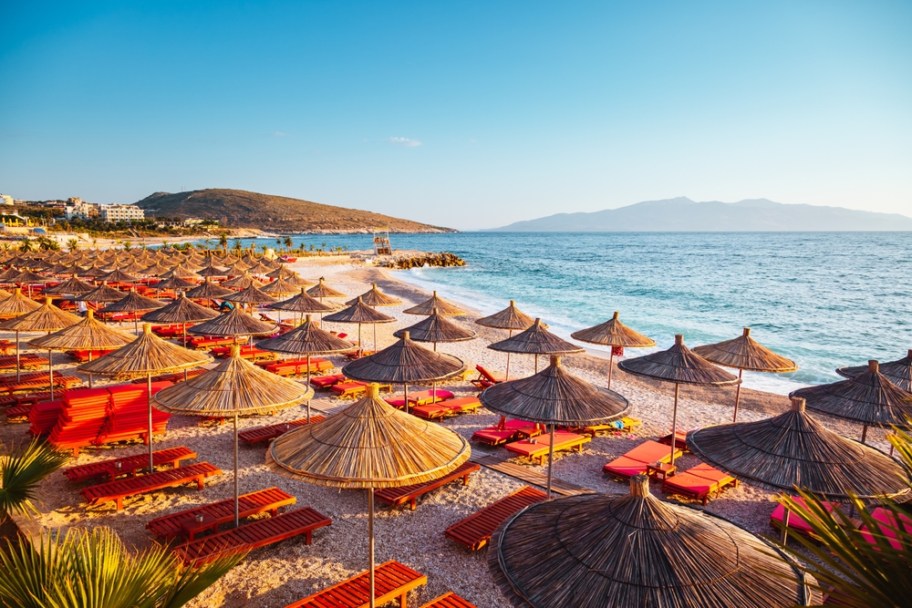 Pláž v Albánii se slaměnými slunečníky a lehátky u moře