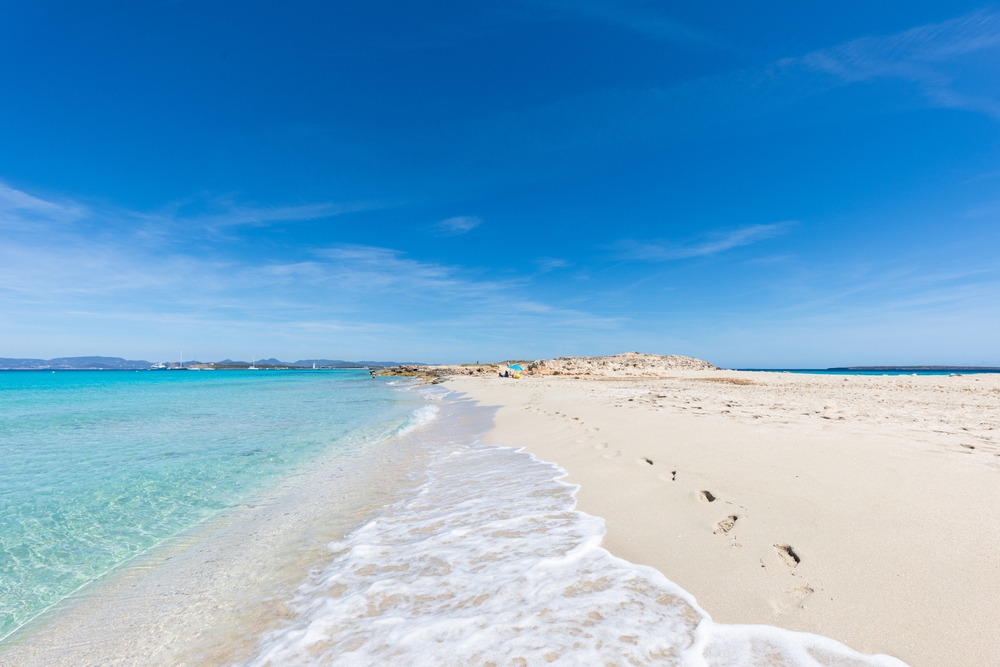 Stopy na písečné pláži na ostrově Formentera u Ibizy s tyrkysovým mořem