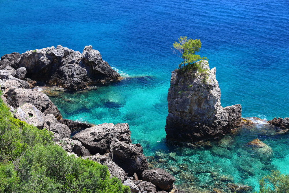 Zářivě modré moře, skály a stromy na pobřeží Paleokastritsy na Korfu