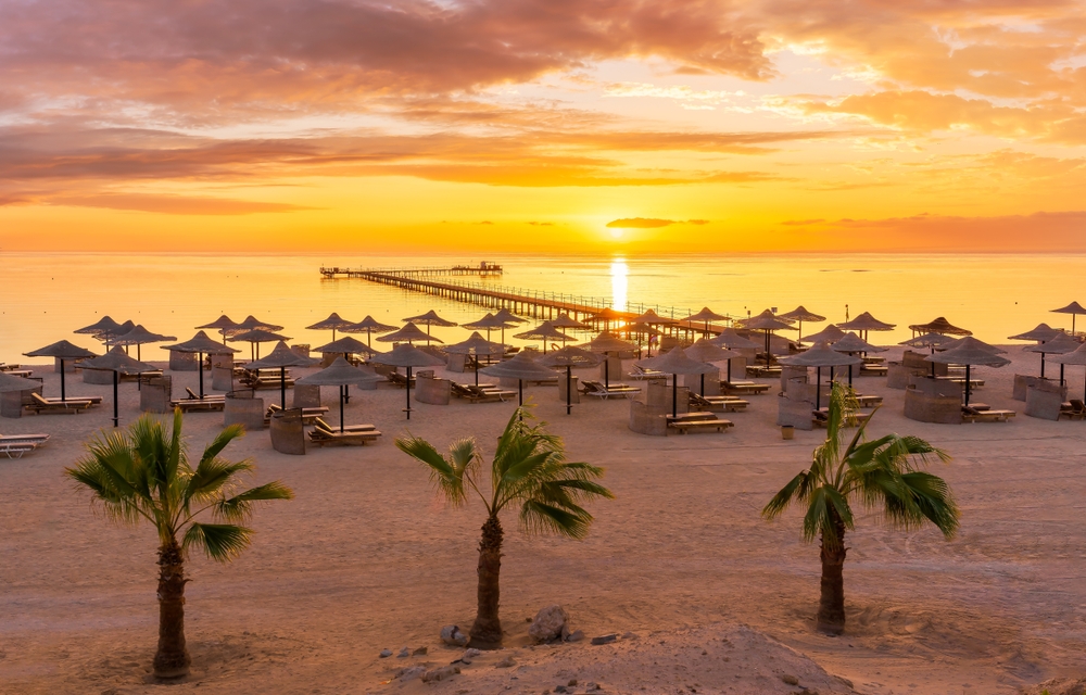 Východ slunce nad pláží v Marsa Alam se slunečníky, lehátky jemným pískem a palmami
