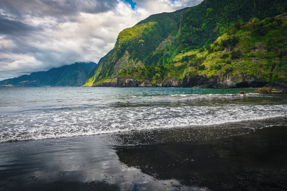 Malebná přímořská scenérie s černou písečnou pláží a klidnými vlnami Atlantského oceánu, Seixal, ostrov Madeira, Portugalsko, Evropa