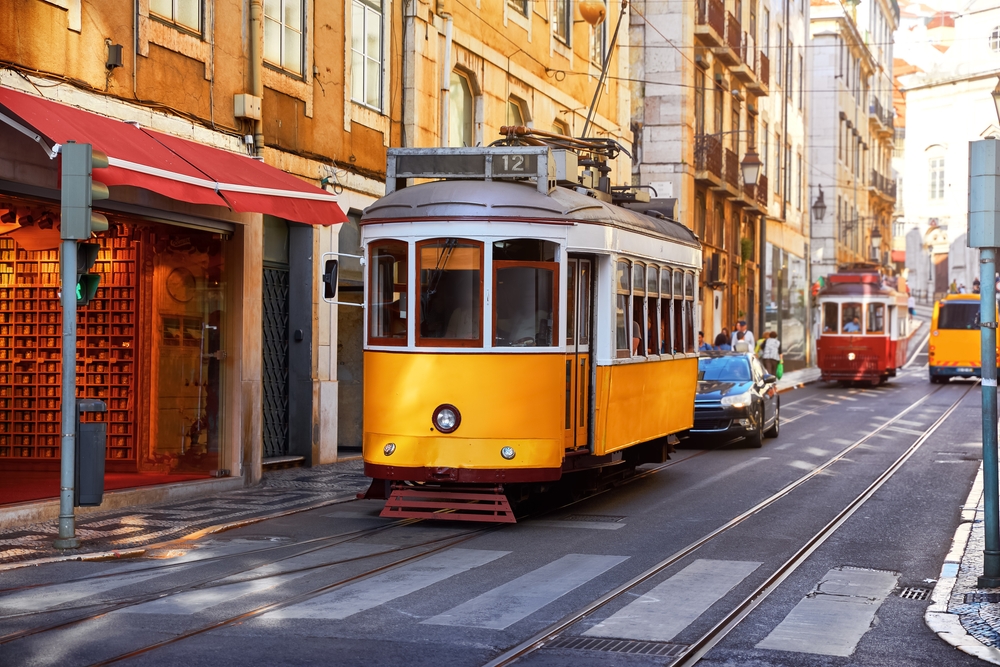 Prodloužené víkendy 2027: Jak nejlépe naplánovat dovolenou? 4 Retro žlutá tramvaj na úzké vedlejší tramvajové trati ve čtvrti Alfama v Lisabonu