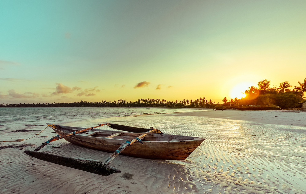 Západ slunce na pláži Pongwe s dřevěnou lodí a palmami v pozadí na Zanzibaru