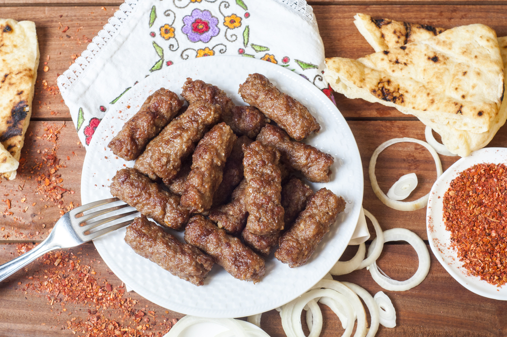 Kebabche, balkánské mleté ​​maso podávané s cibulí, paprikou a chlebem somun na dřevěném pozadí